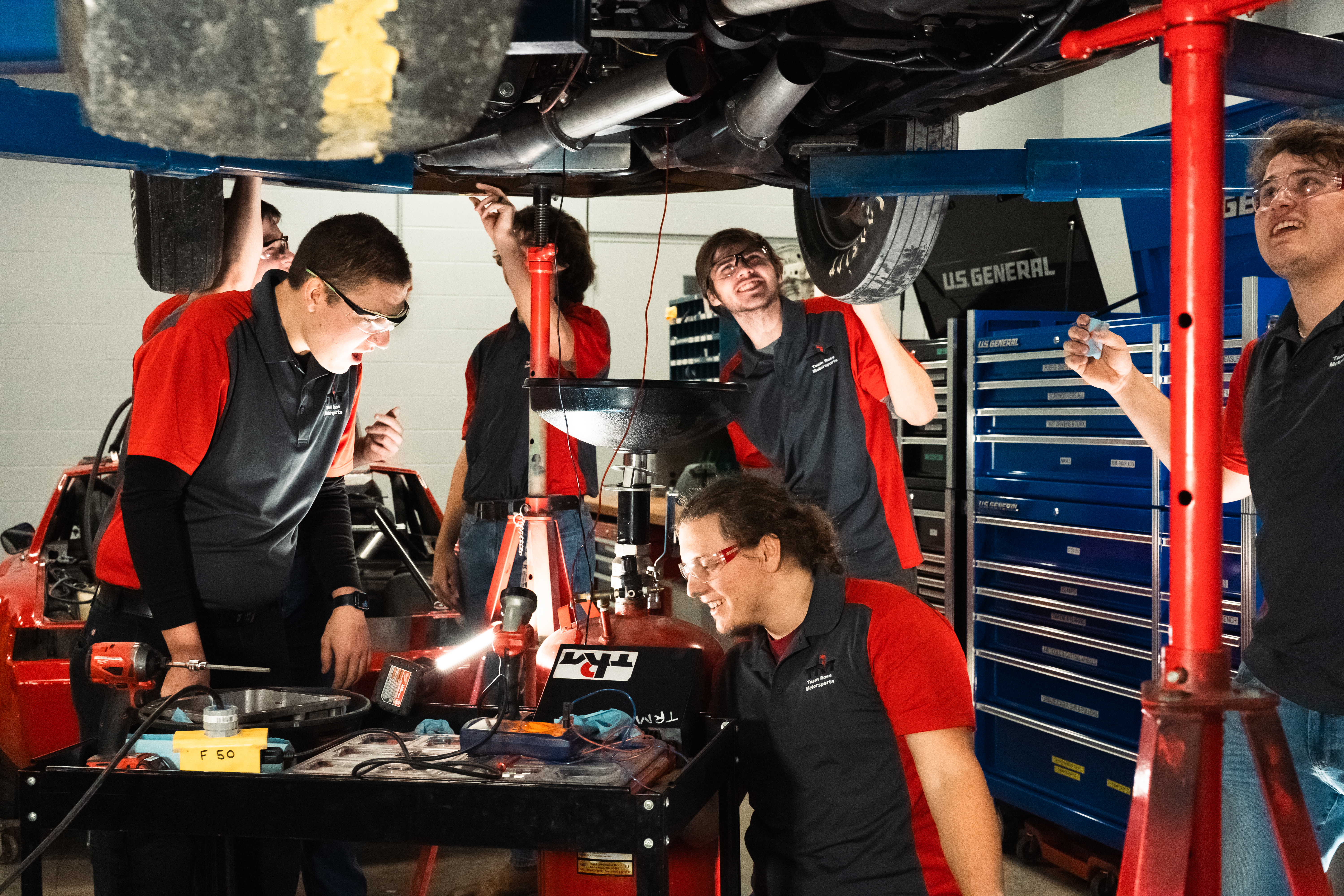 Students work underneath a car on a vehicle lift.
